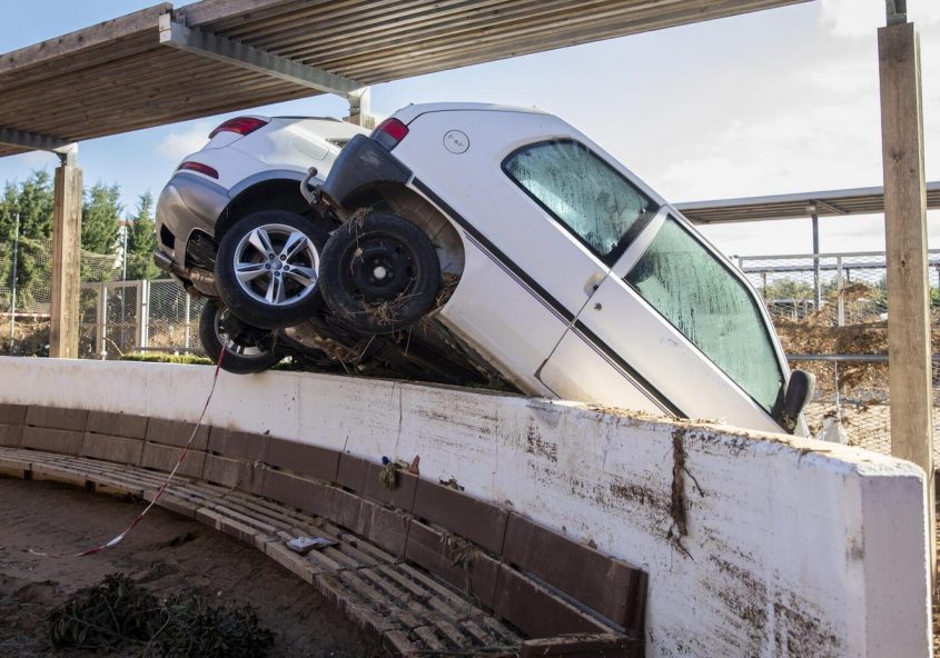 two cars piled on top of a park bench, surrounded by mud and flood debris.